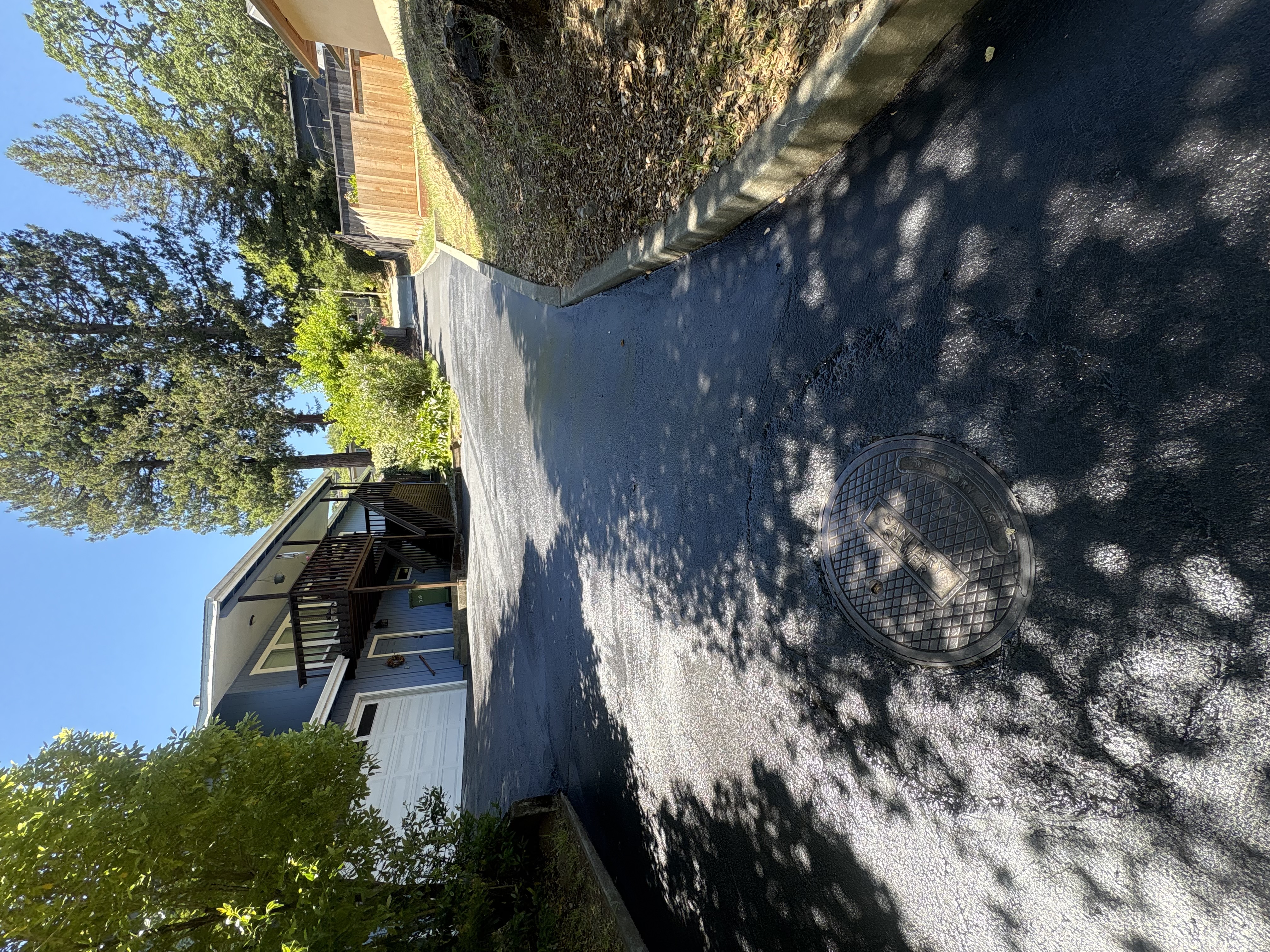 Freshly sealed black driveway after sealcoating with manhole cover